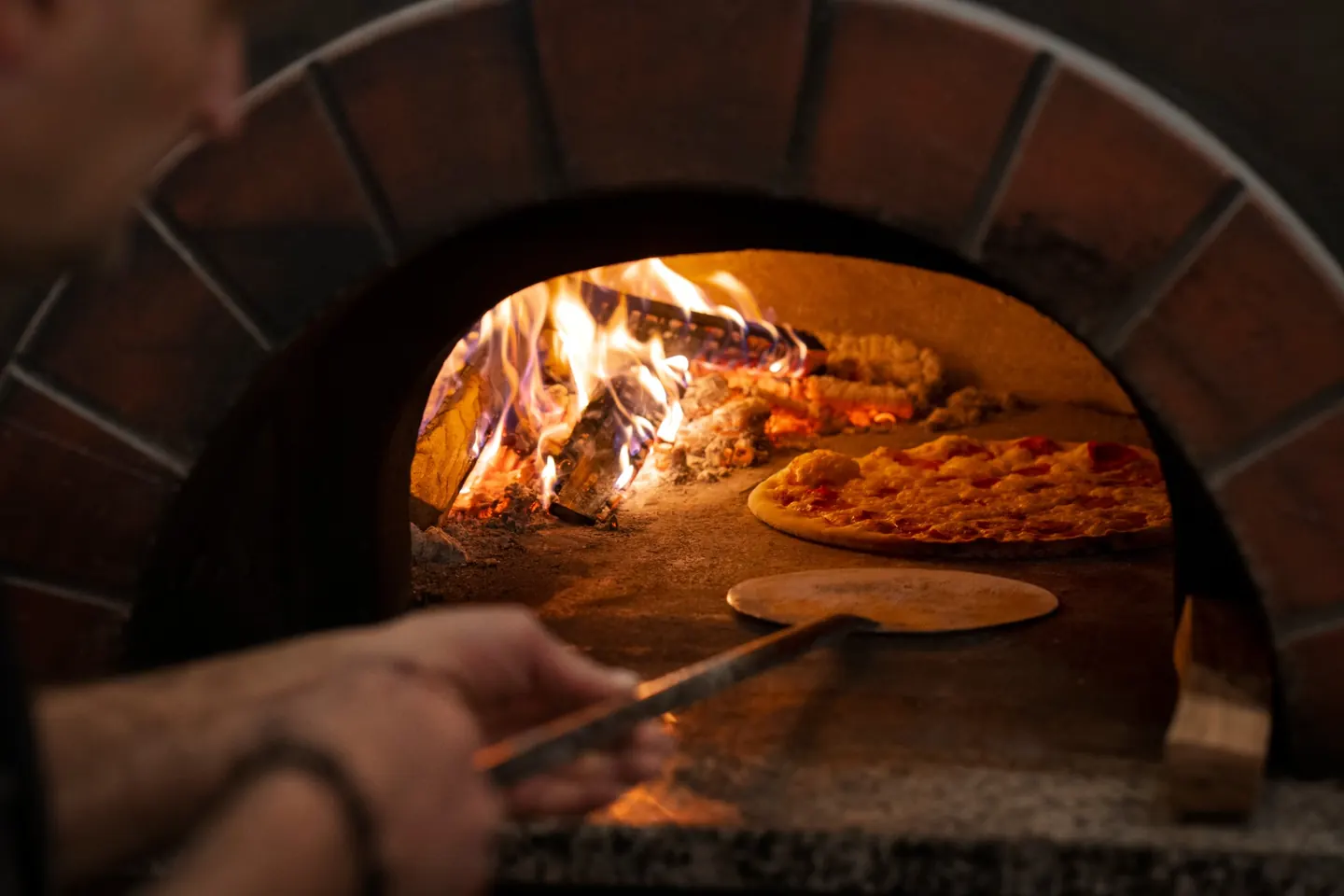 Pizza im Holzofen neben dem offenen Feuer