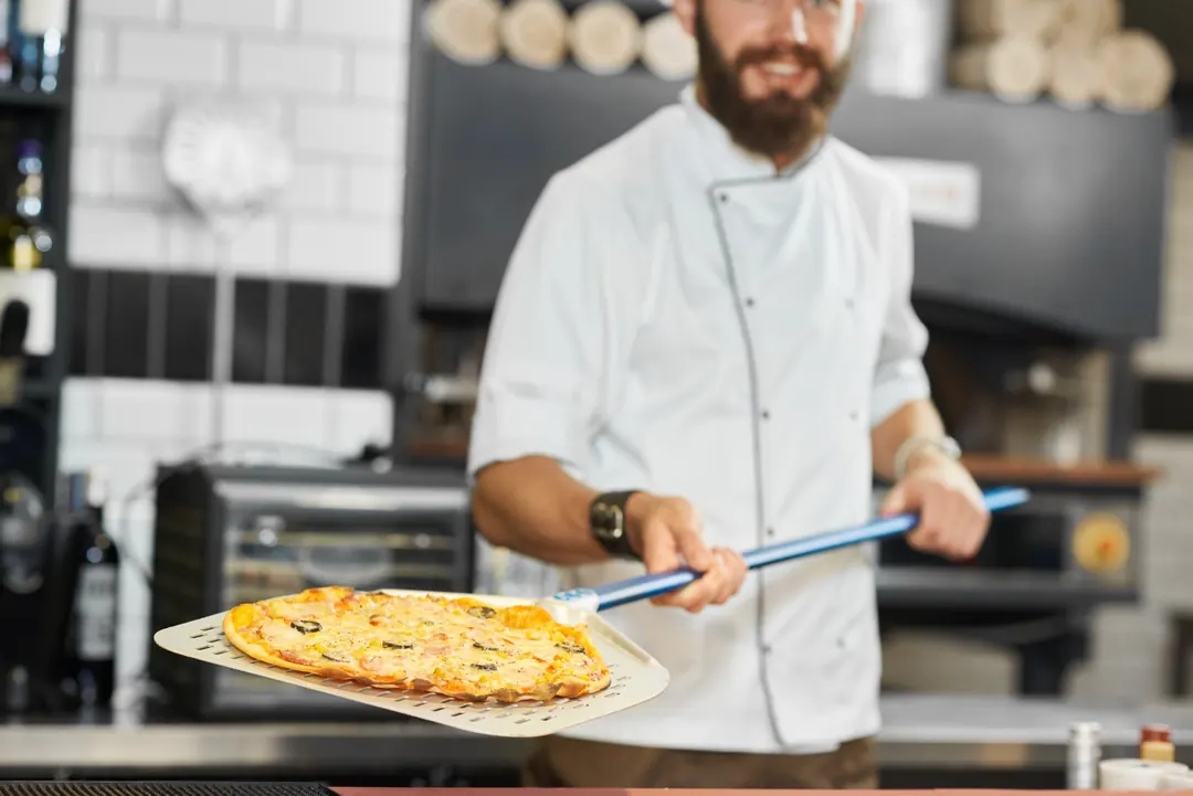 Pizzabäcker zeigt eine frisch gebackene Pizza auf dem Schieber